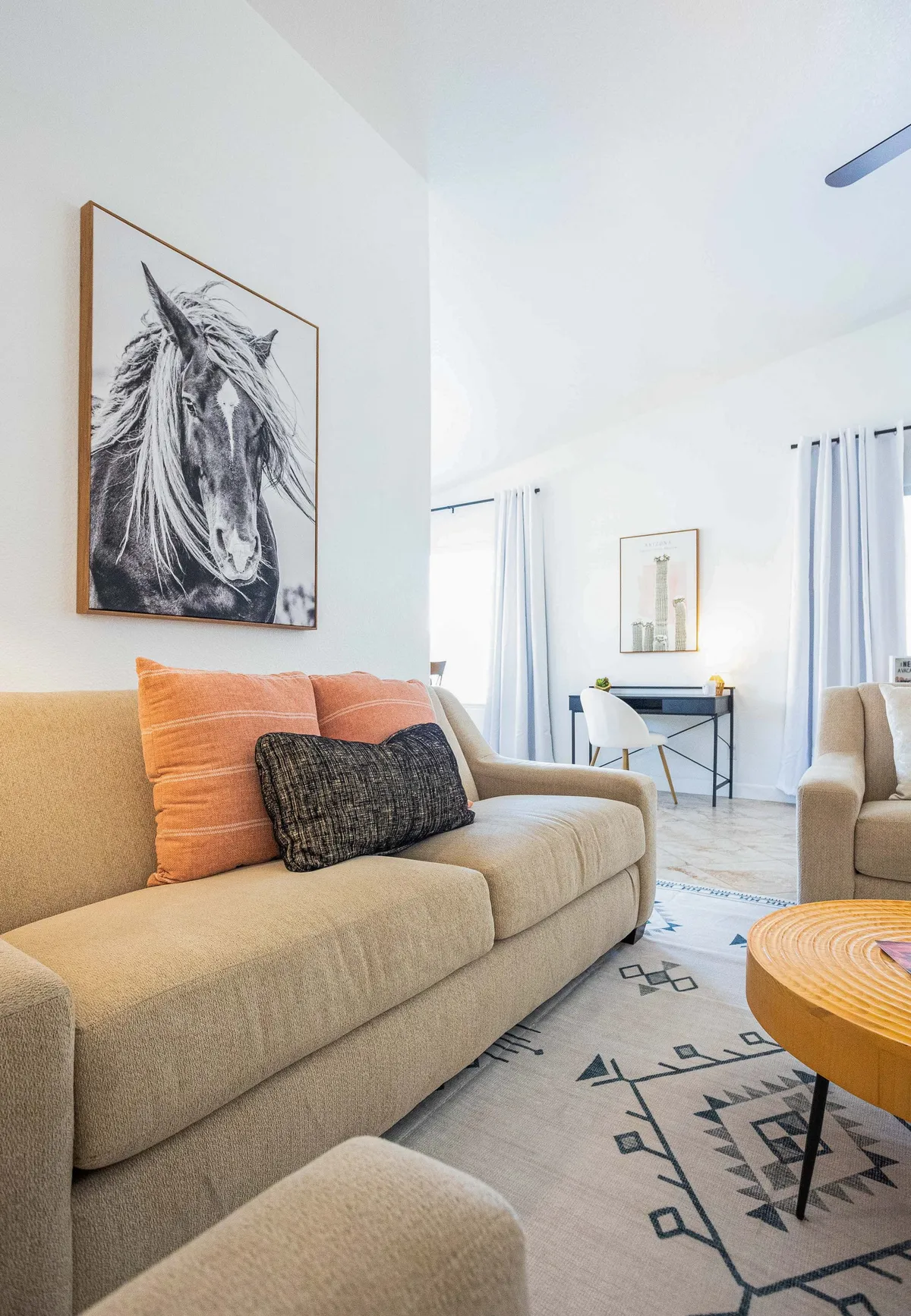 A spacious and inviting common area with a prominent horse portrait, a sofa adorned with colorful pillows, a wooden coffee table, and a decorative rug. The area is well-suited to relaxing, reading, or hosting casual get-togethers.