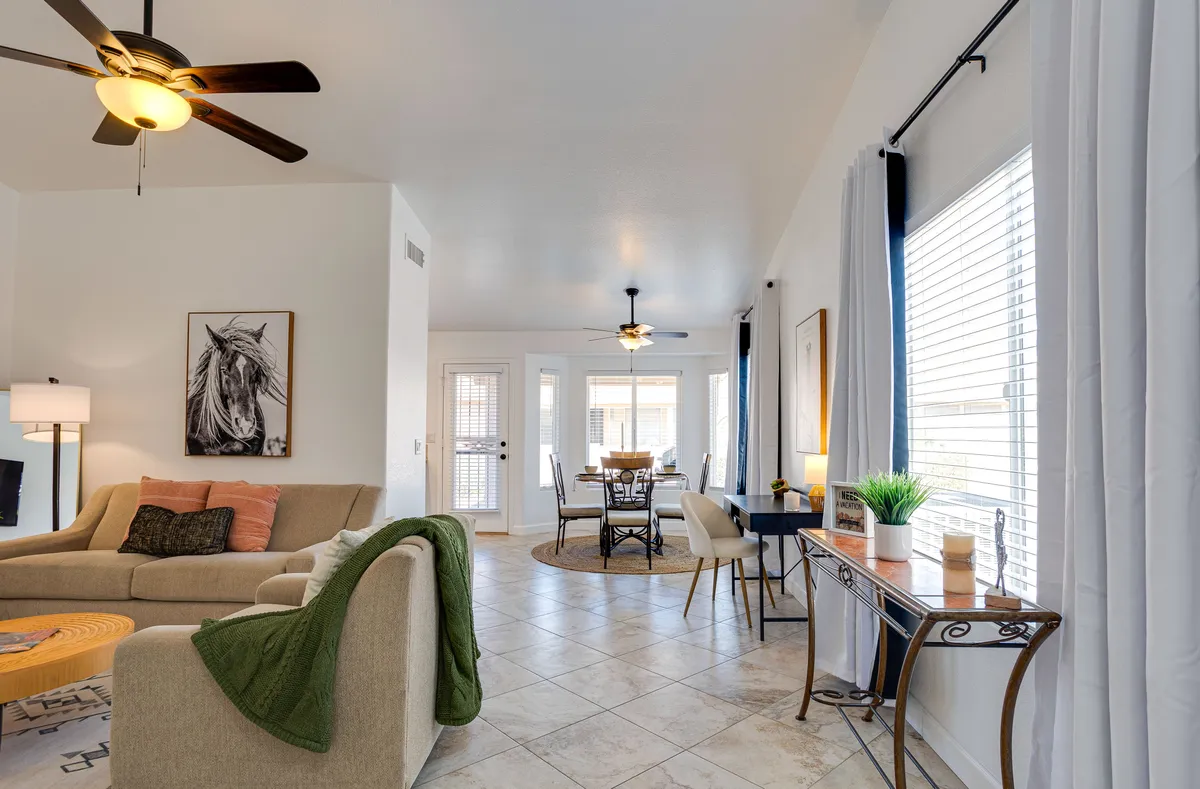 A spacious open-concept living and dining area featuring a comfortable sofa, a wooden dining table with chairs, tasteful wall art, and large windows allowing abundant natural light to fill the room. The seamless layout encourages conversation and social gatherings.