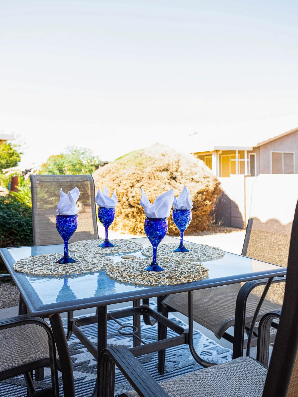 This image displays a cheerful outdoor dining area with blue glasses, white napkins, woven placemats, and a glass table perfect for al fresco meals. The setting suggests both casual gatherings and celebratory events, ideal for enjoying Chandler’s dining scene beyond the home.