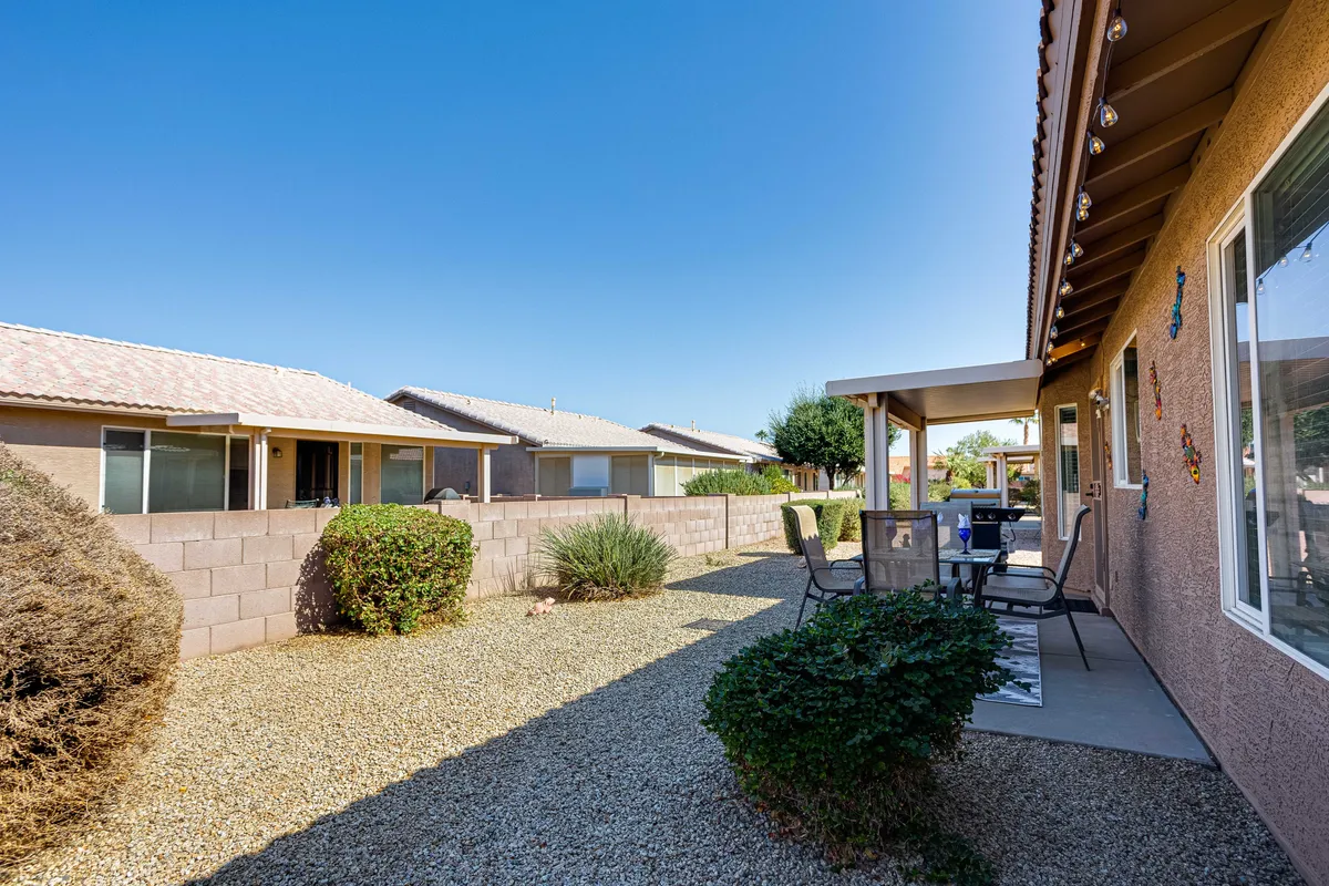 The image shows a tranquil patio space with a gravel pathway, bushes, and an outdoor seating area. The setup is perfect for quiet relaxation, enjoying a meal, or sharing laughter with friends, all in a peaceful garden setting.