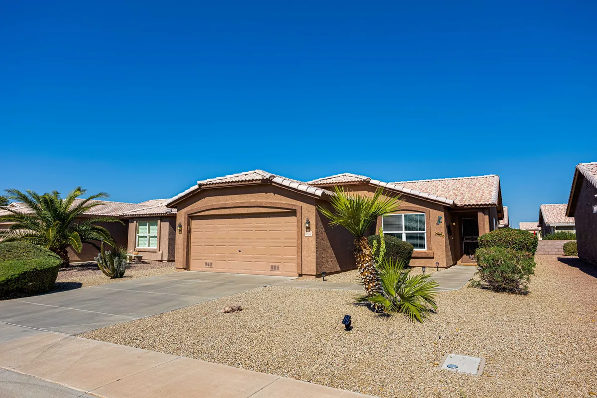 This image shows the inviting front entrance of a home, complete with a well-maintained garage and lush landscaping. The scene suggests a welcoming atmosphere where residents or guests can gather outdoors, socialize, or relax on the porch.